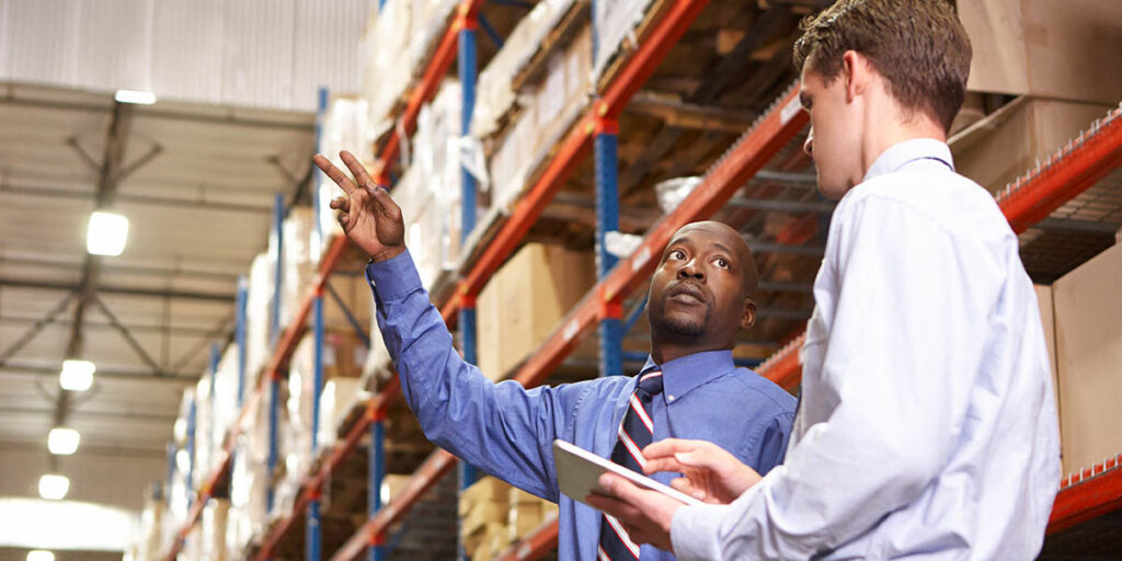 Two businessmen with digital tablet in warehouse.