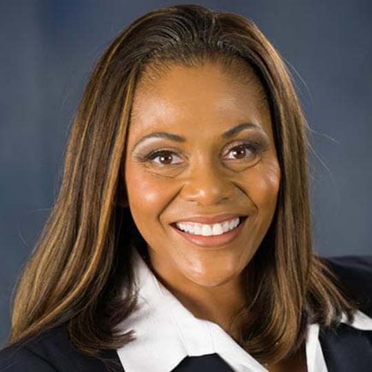 Smiling woman with shoulder length brown hair, wearing a white shirt and black suit jacket.