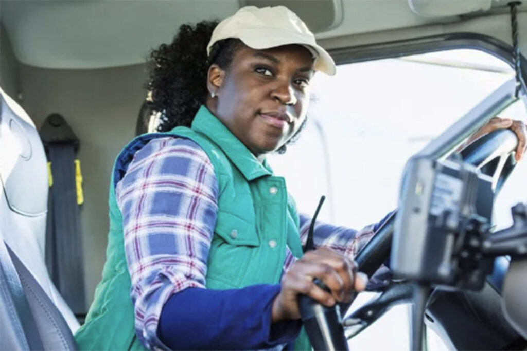 A female truck driver in the cab of her vehicle.