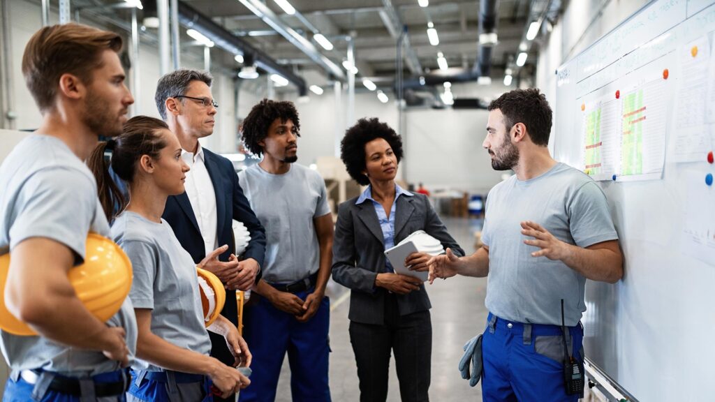 A younger employee leads a team meeting in front of a whiteboard.